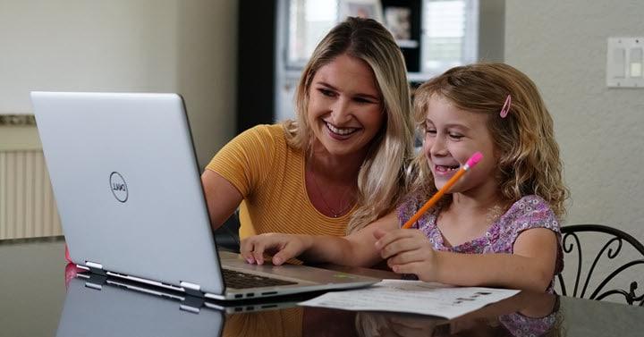 A mother is happily helping her daughter take notes for an online lesson